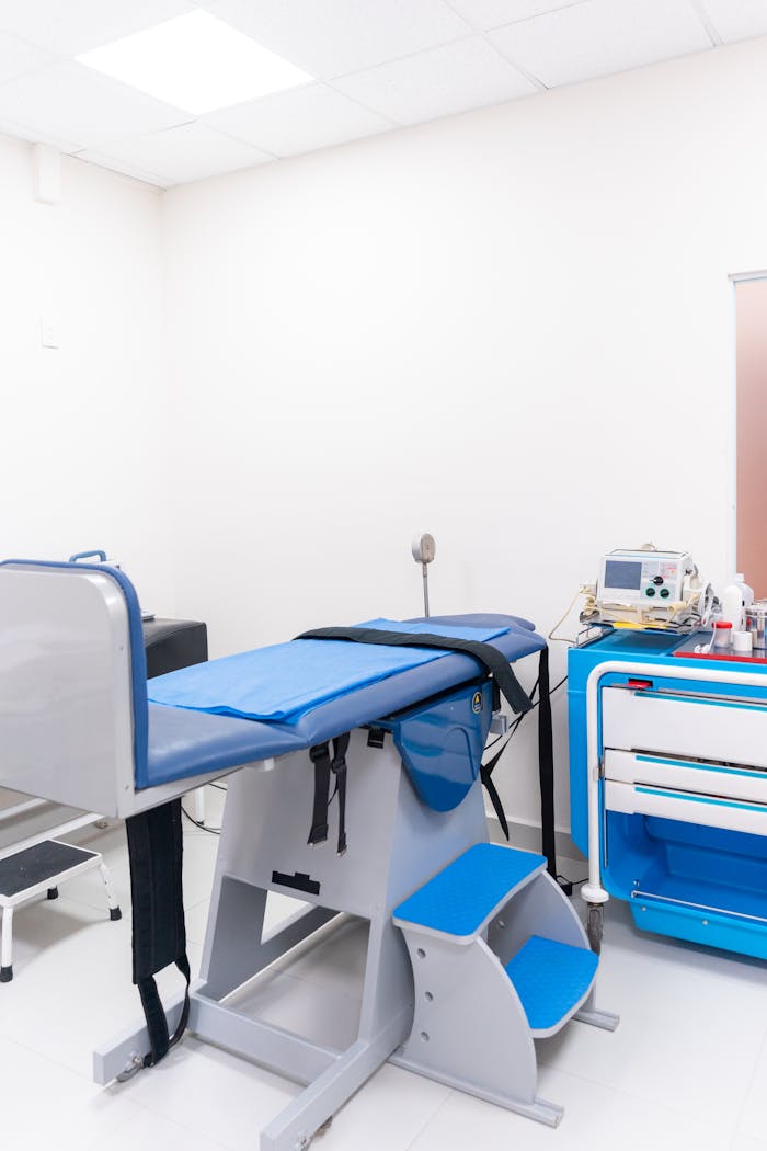 contact-img Clean and well-equipped hospital examination room with blue medical equipment and diagnostic devices.